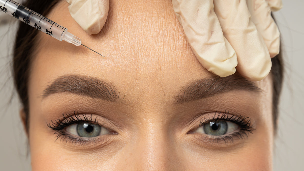 Aplicación precisa de toxina botulínica (bótox) en la frente con manos enguantadas, para suavizar las líneas de expresión y conservar una mirada natural, en El Poblado, Medellín